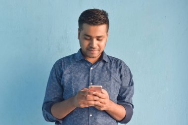 Genç Hintli adam gülümsüyor ve işaret parmağıyla işaret ediyor yarı günlük giysiler içinde açık mavi arka planda yalnız poz veriyor.