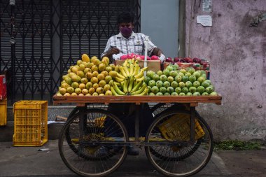 Hintli bir adam Hint sokak pazarında satmak için tezgahlanmış mango gibi meyveler satıyor. 