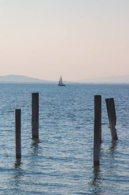 Açık mavi deniz suyunda dikey olarak tahta iskele sütunları ve ufukta gezinen küçük tatil yelkenlisi, deniz üzerinde tatil aktivitesi fikri