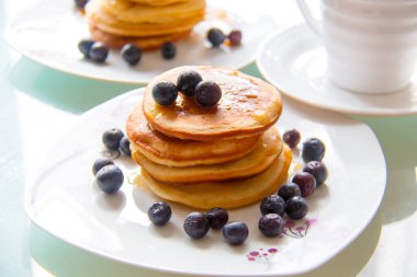 Delicious homemade pancake tower with maple sirup and organic blueberries on the white plate next the cup of coffee. Sweet breakfast pancakes