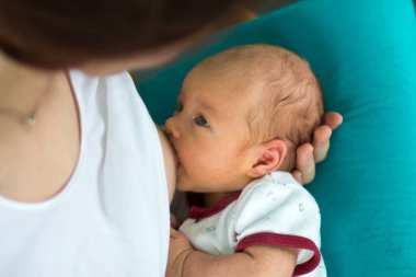 Sevgi dolu bir anne, yeni doğmuş bebeği elinde tutuyor ve emziriyor. Küçük tatlı bebek, mavi arka planda sağlıklı annesinin sütünü emiyor.