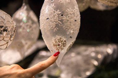 Kırmızı uzun tırnaklı kadın işaret parmağı Noel 'in beyaz kristal şeffaf dekorasyonuna kar taneciklerinin süslemesiyle dokunuyor.