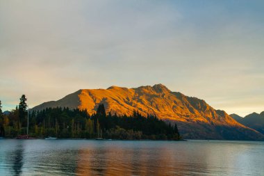 Altın güneşle boyanmış dağ, Wakatipu Gölü 'nün üzerindeki sonbahar ağaçları suyun güzel yansımasıyla Cecil Peak ünlü Queenstown kenti Yeni Zelanda' nın Güney Adası Otago, Otago,