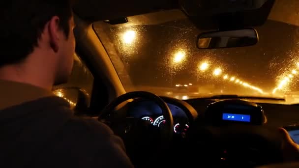 Vista interior de un hombre conduciendo su taxi privado por las calles de la ciudad por la noche — Vídeo de stock