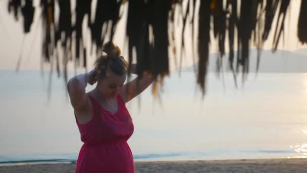 Соблазнительная беременная девушка с длинными волосами позирует на закате на пляже — стоковое видео