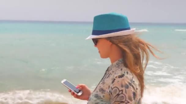 Steadicam disparo de la mujer que utiliza la aplicación en el teléfono inteligente en la playa a pie. Chica usando teléfono inteligente al aire libre con el océano o el fondo del mar — Vídeos de Stock