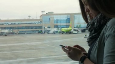 Havaalanı cam duvara bir akıllı telefon kullanan beyaz kadın