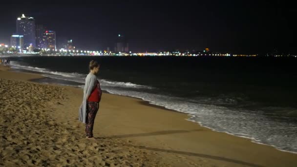 Unga gravida damen på natten stranden ser till havet och sedan gå barfota bort. Stora staden lights i bakgrunden. Nha Trang, Vietnam, Asien. — Stockvideo