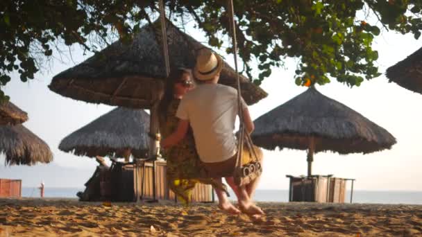 Romantisches Paar, das unter dem Baum am Strand schwingt und miteinander spricht. Sonnenuntergang — Stockvideo