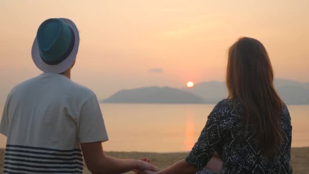 Vista trasera del joven sosteniendo a sus novias de la mano. Pareja sentada en la playa y observando la puesta de sol sobre el mar. Vacaciones tropicales en Vietnam . — Vídeos de Stock