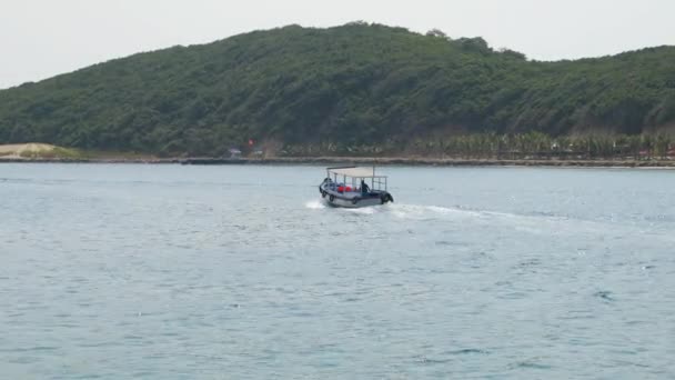 Small blue motorboat with single person aboard in see bay in Vietnam. Woody mountain in the background. — Stock Video