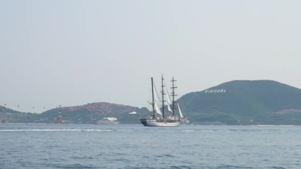 Three mast yacht drifting in the Nha Trang bay, Vietnam. Vinpearl on the background. View from a moving boat. — Stock Video