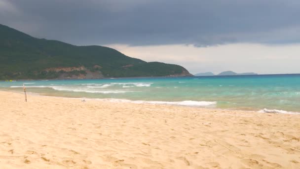 Hermosa vista de la playa de arena y agitando el agua azul del mar con el cielo tormentoso en el fondo — Vídeos de Stock