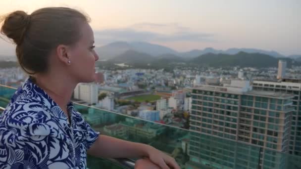 Menina caucasiana olhando para a cidade de Nha Trang, Vietnã, ao pôr-do-sol — Vídeo de Stock