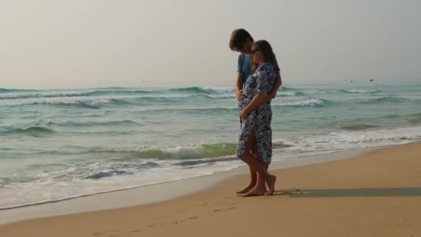 Una pareja caucásica se abraza en la orilla del mar. Hombre acariciando el vientre de sus esposas embarazadas. Espléndido paisaje marino . — Vídeo de stock