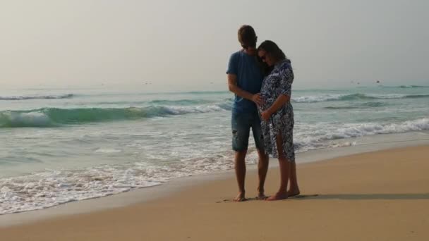 해변에서 행복 한 커플 기대 아기입니다. 젊은 남자 애 무 웃는 여 대 배와 안에 아기와 이야기. — 비디오
