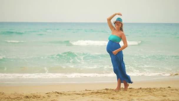 Mladá těhotná žena na pláži na větrný den pózuje, zvedá ruce a s úsměvem — Stock video