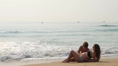 Hamile kadın ve deniz suyu yakınındaki bir kum plajı üzerinde yatan adam. Onları sıçramasına dalgalar.