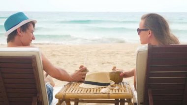 Taze hindistan cevizi içme beach longers tatlı genç çift. Mavi denizi ve beyaz kum arka planda sallayarak