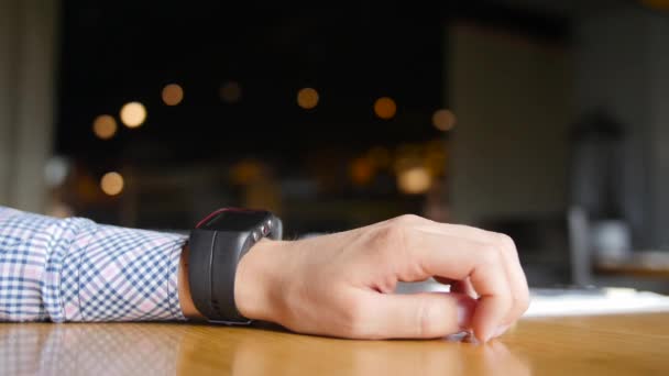 Man sitter på ett café och använder sin smarta klocka. På nära håll beskåda av händer — Stockvideo