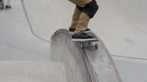 Joven patinador con rodilleras saltando sobre una cornisa en un parque de skate — Vídeos de Stock