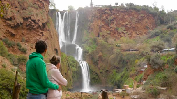Paret tittar på majestätiska Ouzouds vattenfall. Man och kvinna besöker kända turistattraktion Marocko. Man och kvinna njuter av sin semester avkopplande efter vandring. — Stockvideo