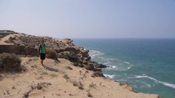 Hombre joven caminando sobre hermosas dunas inspiradoras del desierto en el soleado día de verano, fondo marino — Vídeo de stock