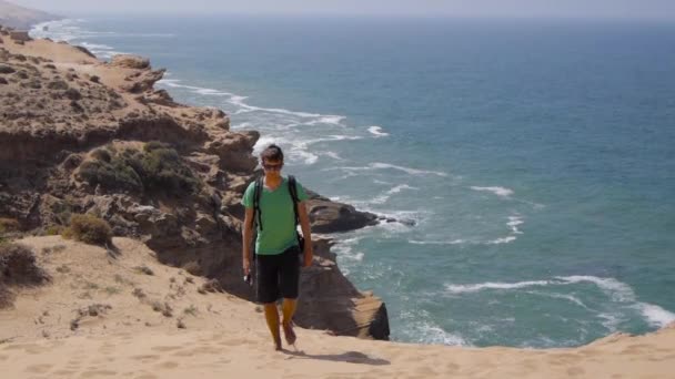 若い男は、日当たりの良い夏の日、海の背景に美しい感動的な砂漠の砂丘にクロスします。 — ストック動画