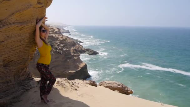 Uma jovem mulher bonita ficar perto de rocha mais de tirar o fôlego vista fundo do oceano — Vídeo de Stock