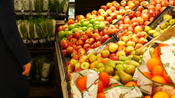 Женщина в супермаркете подходит к фруктовому прилавку. Она выбирает яблоки — стоковое видео