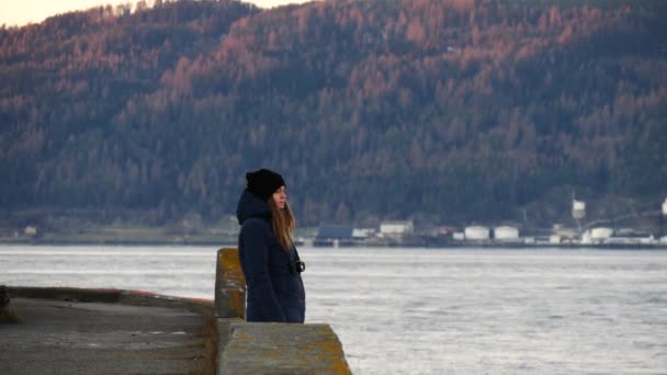 Kaukasische vrouw met camera standin op de kade van een zee en zonsondergang te wachten. Fjord in Trondheim, Noorwegen. — Stockvideo