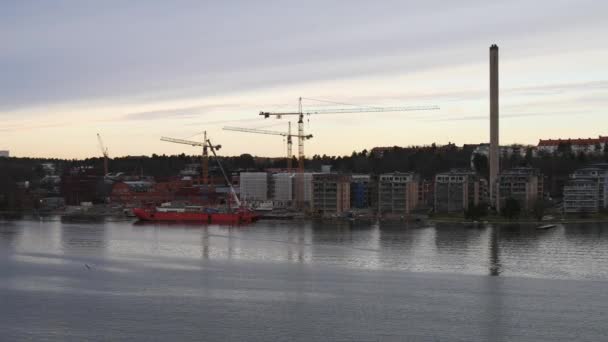 Floating on the river by buildings, tower cranes and red ship — Stock Video