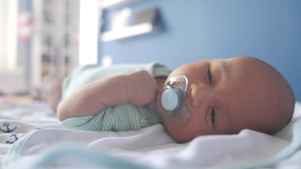 Porträt eines schläfrigen Babys, das ein Beruhigungsmittel in einem Bett saugt — Stockvideo