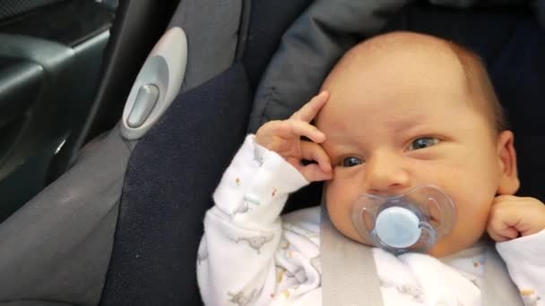 Kalm slaperig baby in een kinderzitje voor de veiligheid in de auto. Bany zuigen fopspeen — Stockvideo