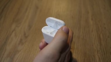 Erkek eli, kablosuz kulaklığı beyaz şarj çantasına yerleştirdi. Yakın çekim.