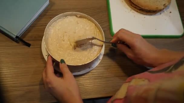 Eine Bäckerin macht sogar eine Schicht süße Sahne auf einem Kuchen in einer runden Form. Ansicht von oben — Stockvideo