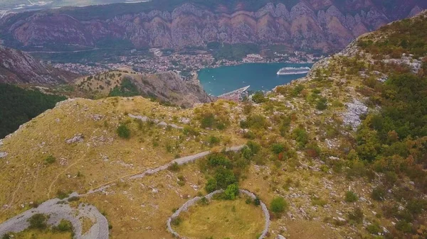 Dağlar arasında sahil kasabasını gören bir manzarayla tepenin üzerinden uçmak. Karadağ 'ın Kotor Körfezi Havalimanı