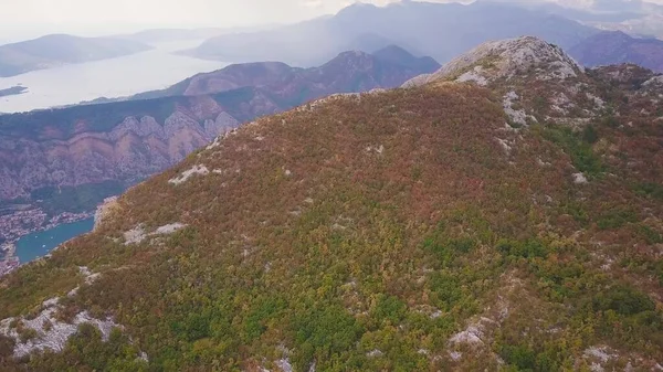 Dağlar arasında kıyı kasabasını gören bir manzarayla tepenin üzerinden uçuyor. Karadağ 'ın Kotor Körfezi Havalimanı