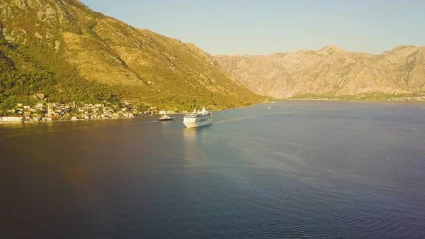 Lüks yolcu gemisi güneşli dağlara karşı deniz koyunda yüzüyor. Karadağ 'ın Kotor Körfezi havadan görünüşü