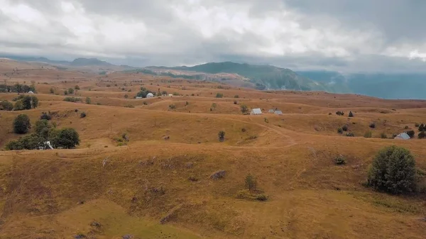 Yukarda kuru otlarla kaplı tepelik bir plato. Bulutlar dağların tepelerini kaplar