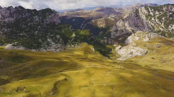 Sarı tepeler ve Dinarik Alplerin kayalık tepeleri. Güneş ışığı bulutlardan gölgeler salıyor. Havadan