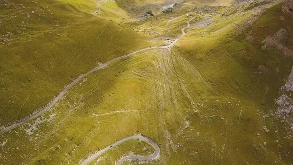 Güneşli dağ geçidinde dolambaçlı bir yol. Sarı yamaçlardaki bulutların gölgeleri. Havadan