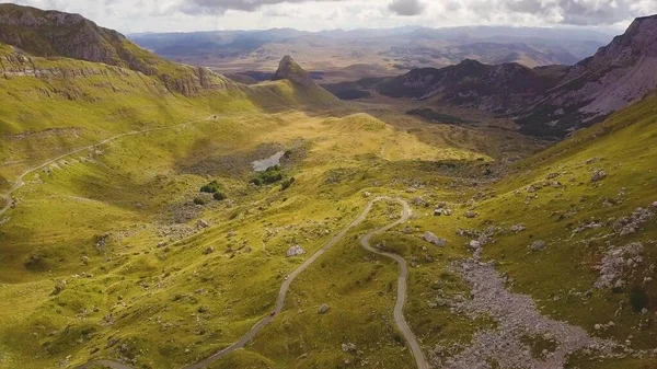 Yukarı geçitte dar dağ yolu. Bulutların gölgeleri güneşli yamaçlarda hareket eder. Havadan