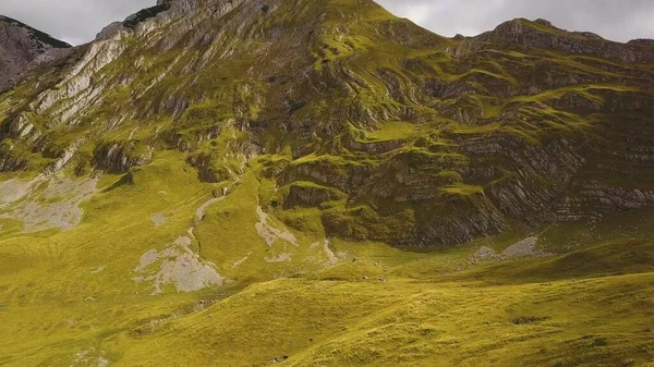 Bir sürü jeolojik katları olan güneşli çimenli dağın havadan görünüşü. Gölgeler dik yamaçta hareket eder