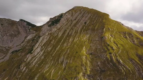Jeolojik kıvrımlarla güneşli çimenli bir zirve. Gölgeler dağda hareket eder. Hava görünümü