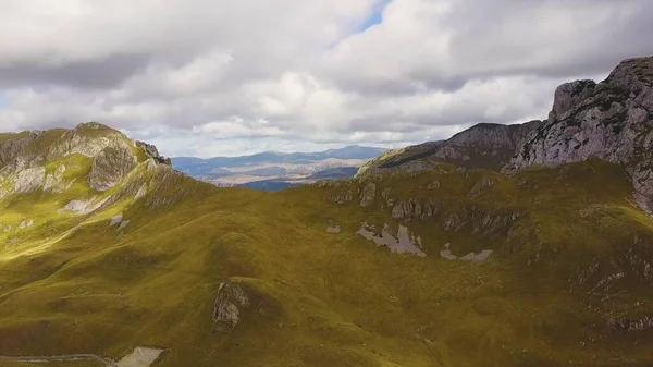 Kavisli dağ yolu ve bulutların gölgeleriyle çimenli tepelerin üzerindeki kayalar. Hava görünümü