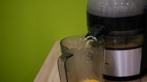 Slow motion het SAP uit de juicer wordt gegoten in een beker. Close-up. — Stockvideo