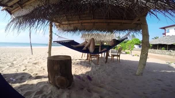 Frau entspannt sich in Hängematte im Schatten der Palmen am tropischen Strand — Stockvideo