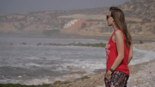 Giovane donna in piedi sulla spiaggia dell'oceano guardando sulle onde. 4K UHD — Video Stock
