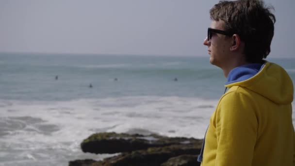 Młody człowiek, stojąc na plaży oceanu patrząc na fale. 4k Uhd — Wideo stockowe